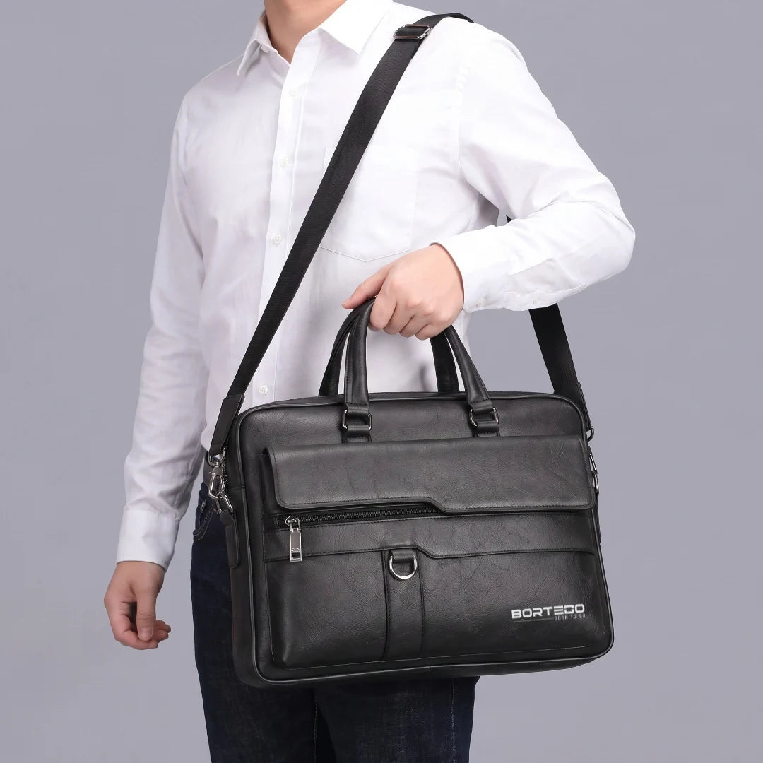 A man wearing a white button-down shirt and dark jeans carries a black leather briefcase-style shoulder bag with top handles and a long shoulder strap against a plain light gray studio background. The bag has a front zip pocket and a visible BORTEGO logo near the lower right corner.