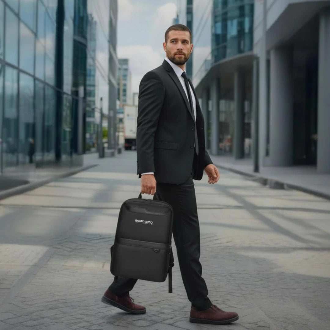 Man in a suit holding a black backpack on a city street.