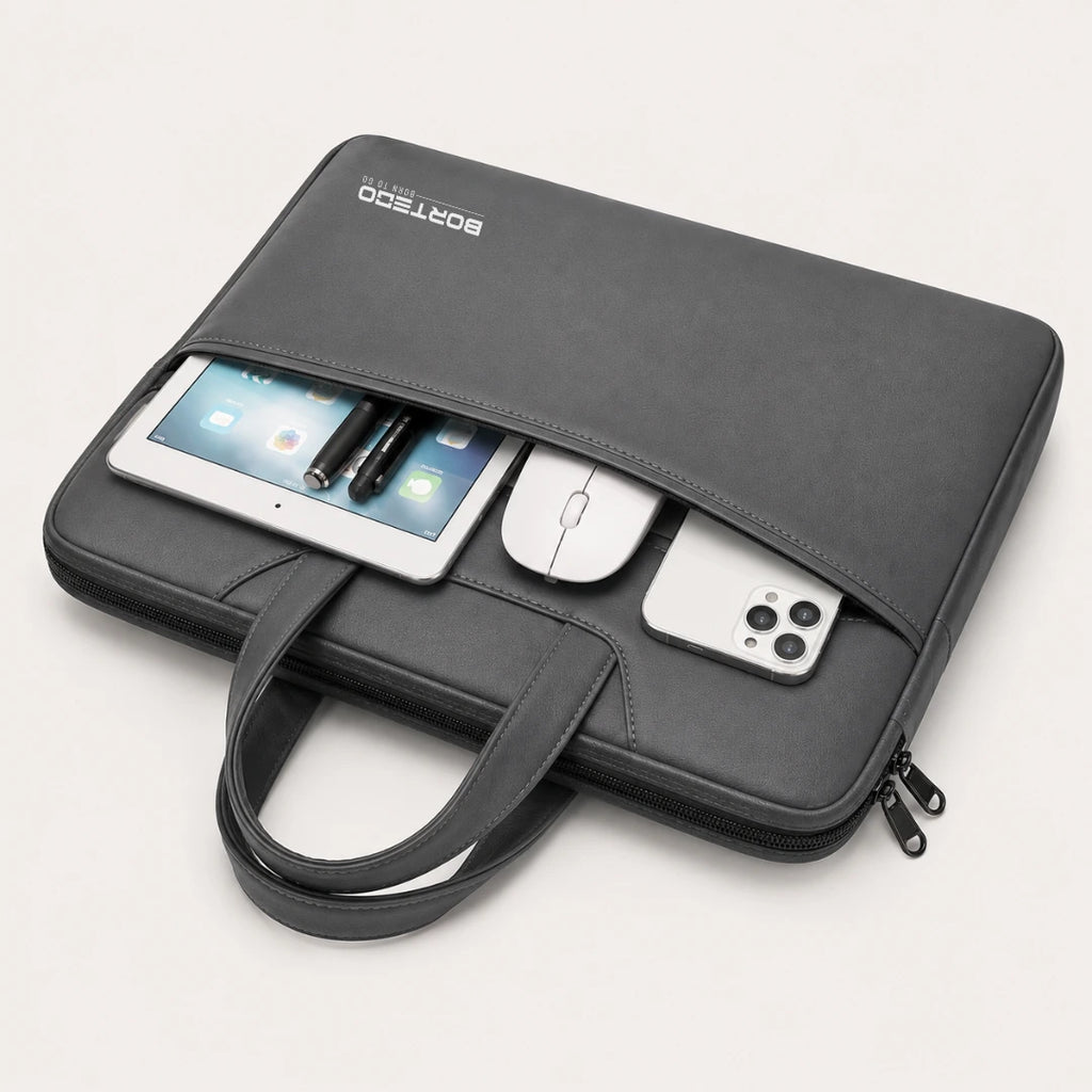 A black laptop sleeve with a top handle, shown on a light beige background. The sleeve is open, displaying a tablet, mouse, and smartphone inside its pockets.