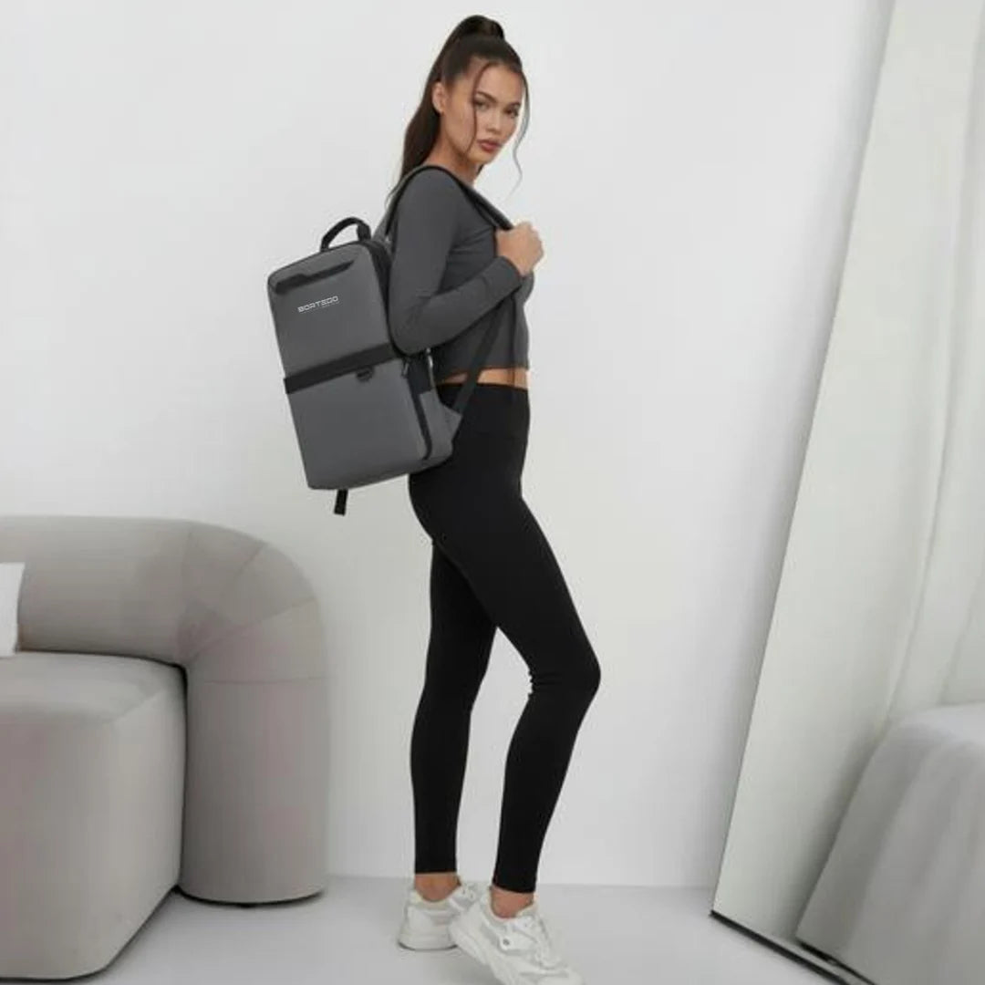 Woman wearing a gray backpack in a minimalistic room.