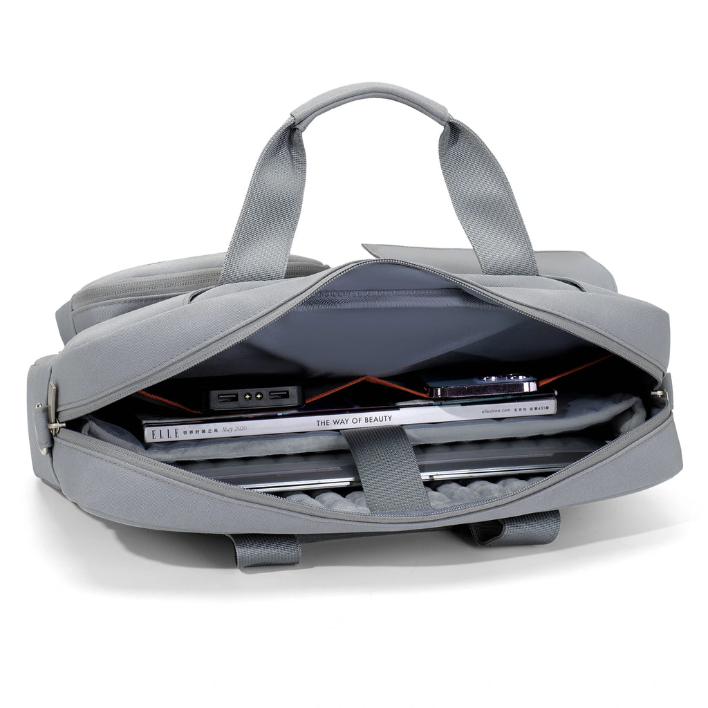 A gray laptop backpack shown open, revealing a padded interior with a laptop, books, and accessories inside. The backpack has dual top handles and is photographed on a clean white background.