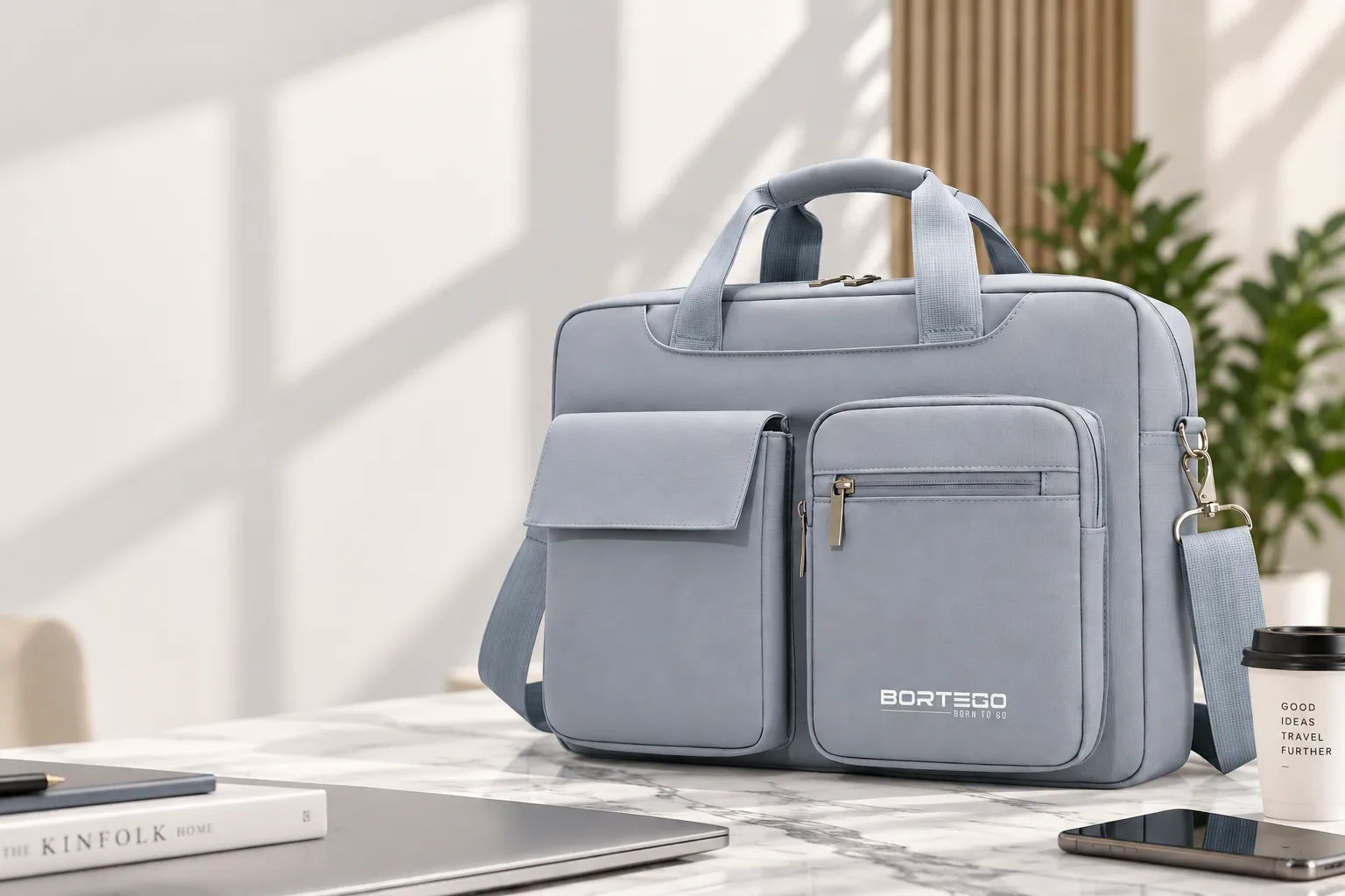 A light blue BORTEGO laptop briefcase with multiple front pockets and top handles, styled on a marble desk with a laptop, phone, and coffee cup nearby.