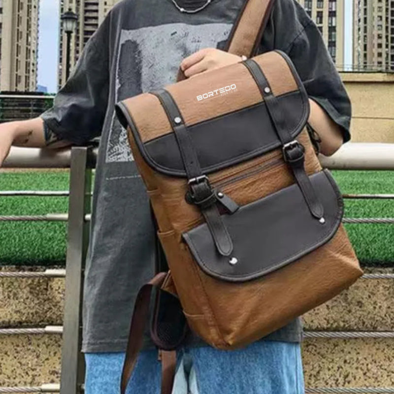 Person holding a brown and black backpack Bortego with 'Bortego' branding outdoors.
