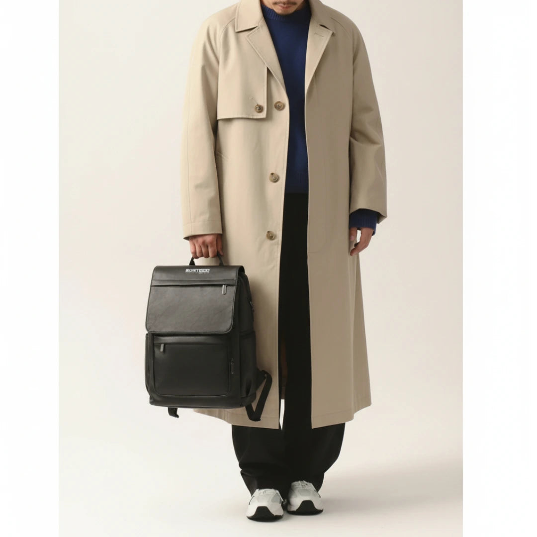 Person wearing a beige trench coat holding a black backpack on a plain background