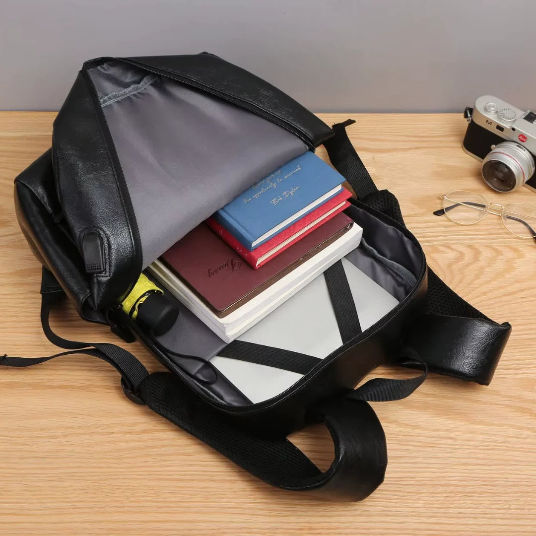 Black backpack Bortego with books and a camera on a wooden surface