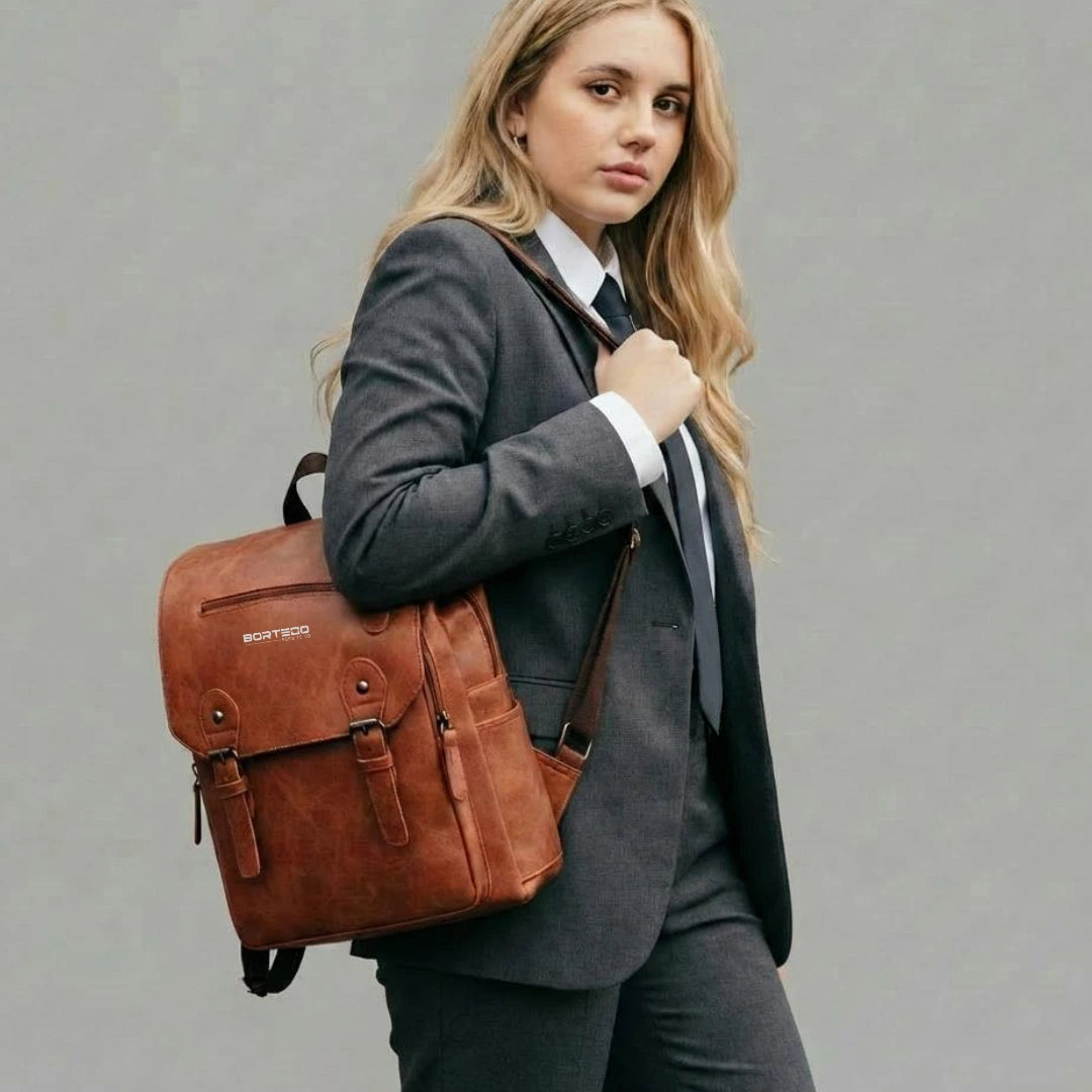 Woman in a suit holding a brown leather backpack against a gray background