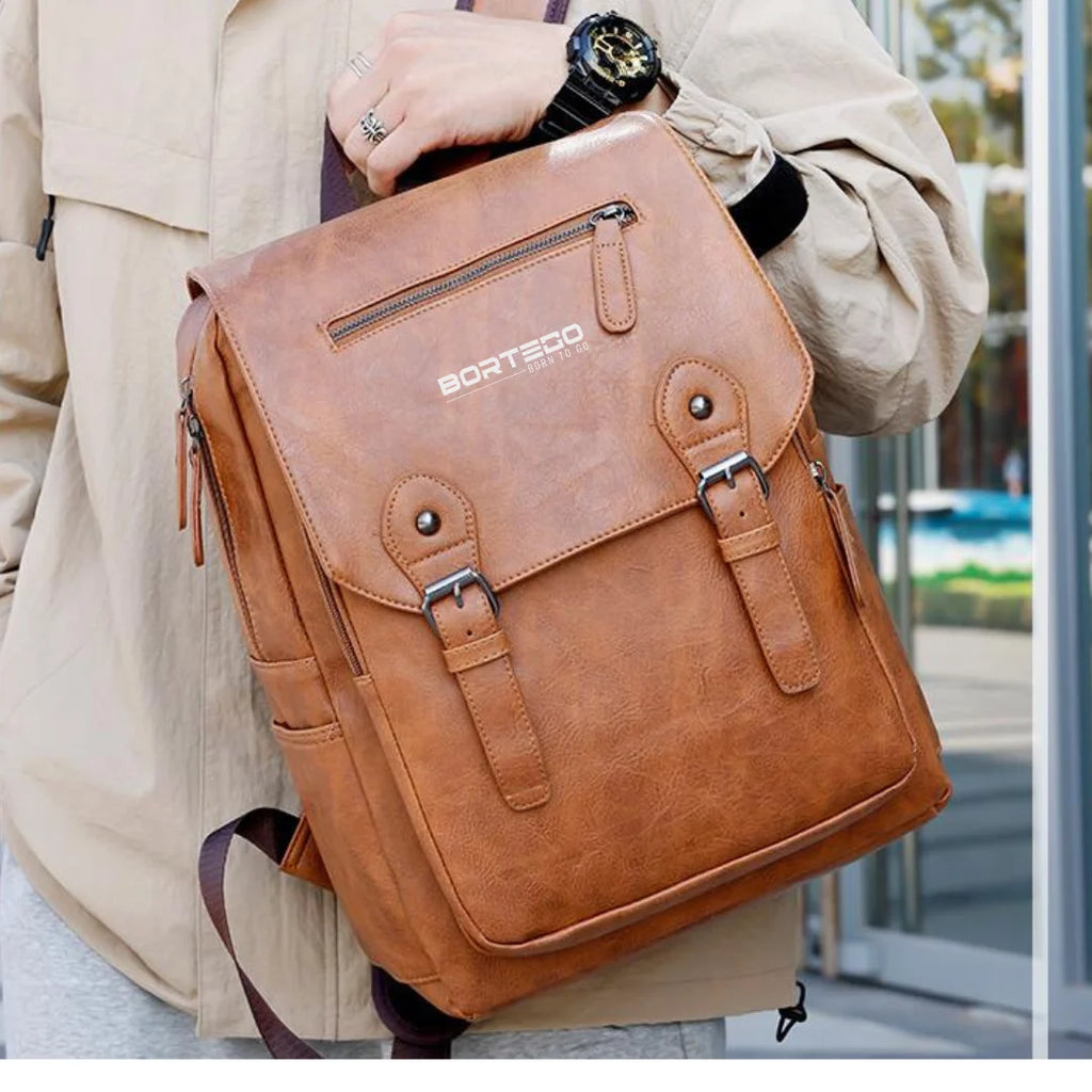 Brown leather backpack held by a person with a blurred background