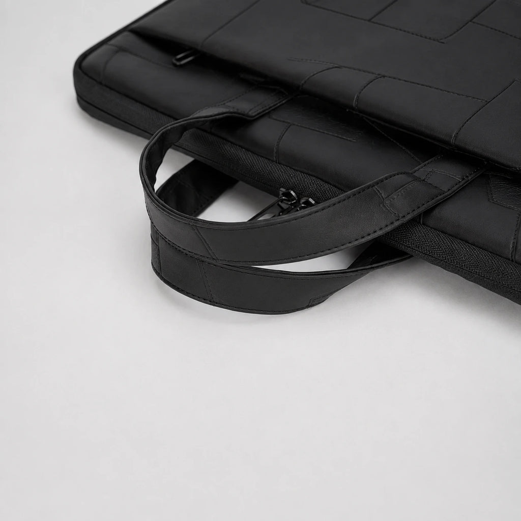Close-up of a black laptop sleeve with a padded shoulder strap and zippered pocket, photographed on a light gray background.