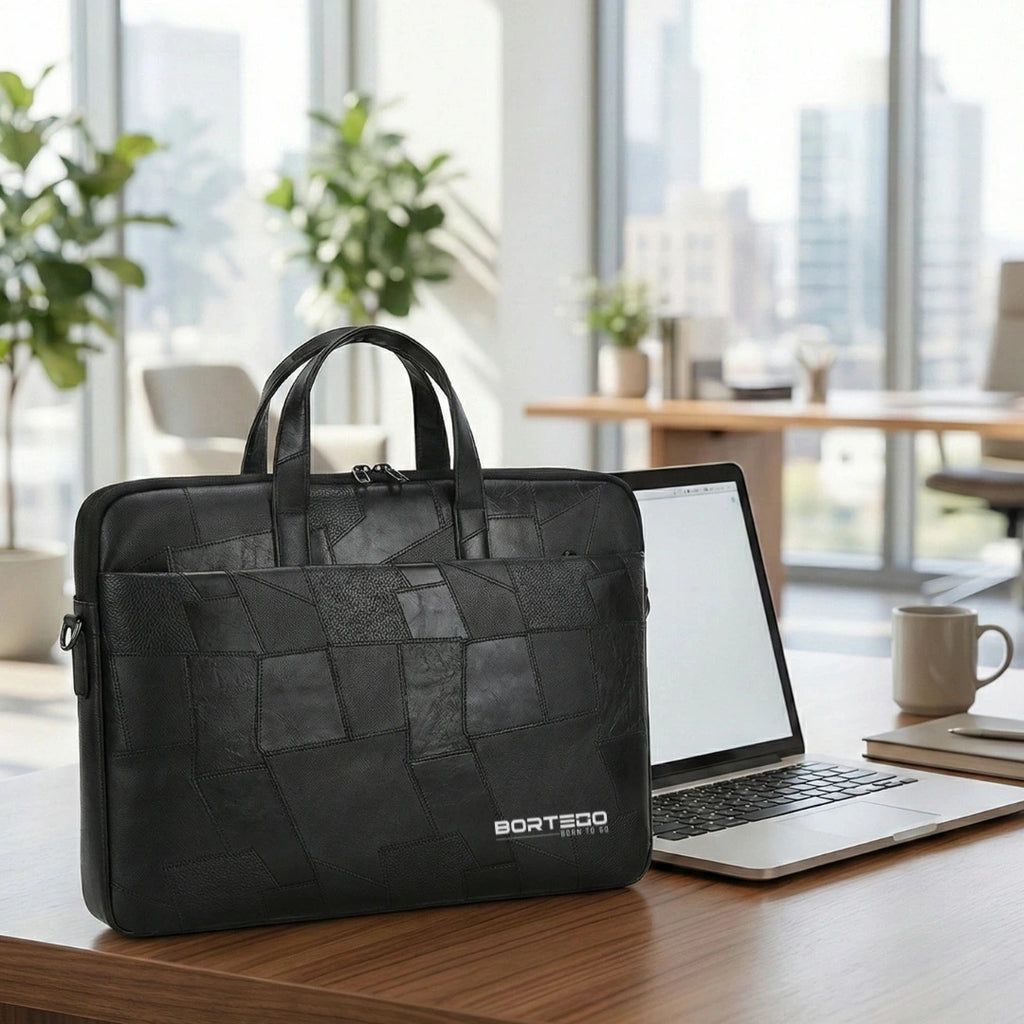 A black BORTEGO laptop briefcase with a textured geometric patchwork pattern, sitting on a wooden desk next to an open laptop in a modern office setting.
