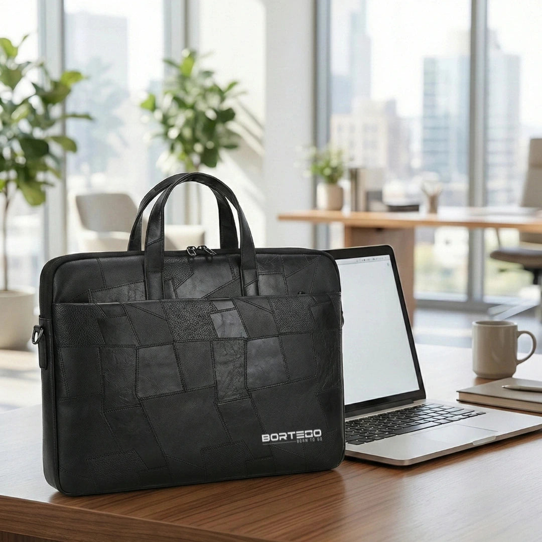 A black BORTEGO laptop briefcase with a textured geometric patchwork pattern, sitting on a wooden desk next to an open laptop in a modern office setting.