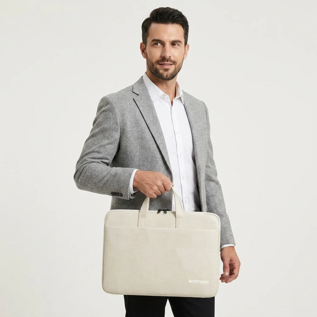 A man in a gray blazer and white shirt holds a light beige fabric laptop sleeve with top handles against a plain light gray studio background.