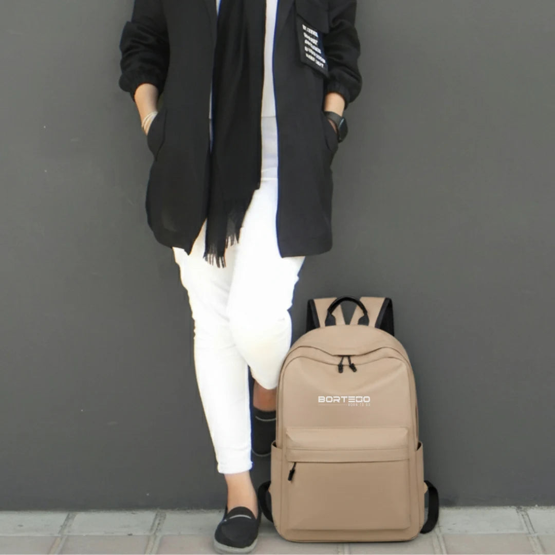 Person wearing a black coat and white pants with a beige backpack on a gray background