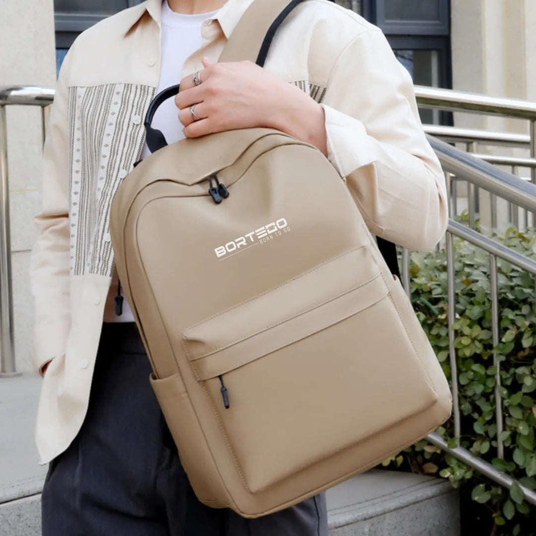 Person holding a beige backpack with 'Bortego' branding outdoors.