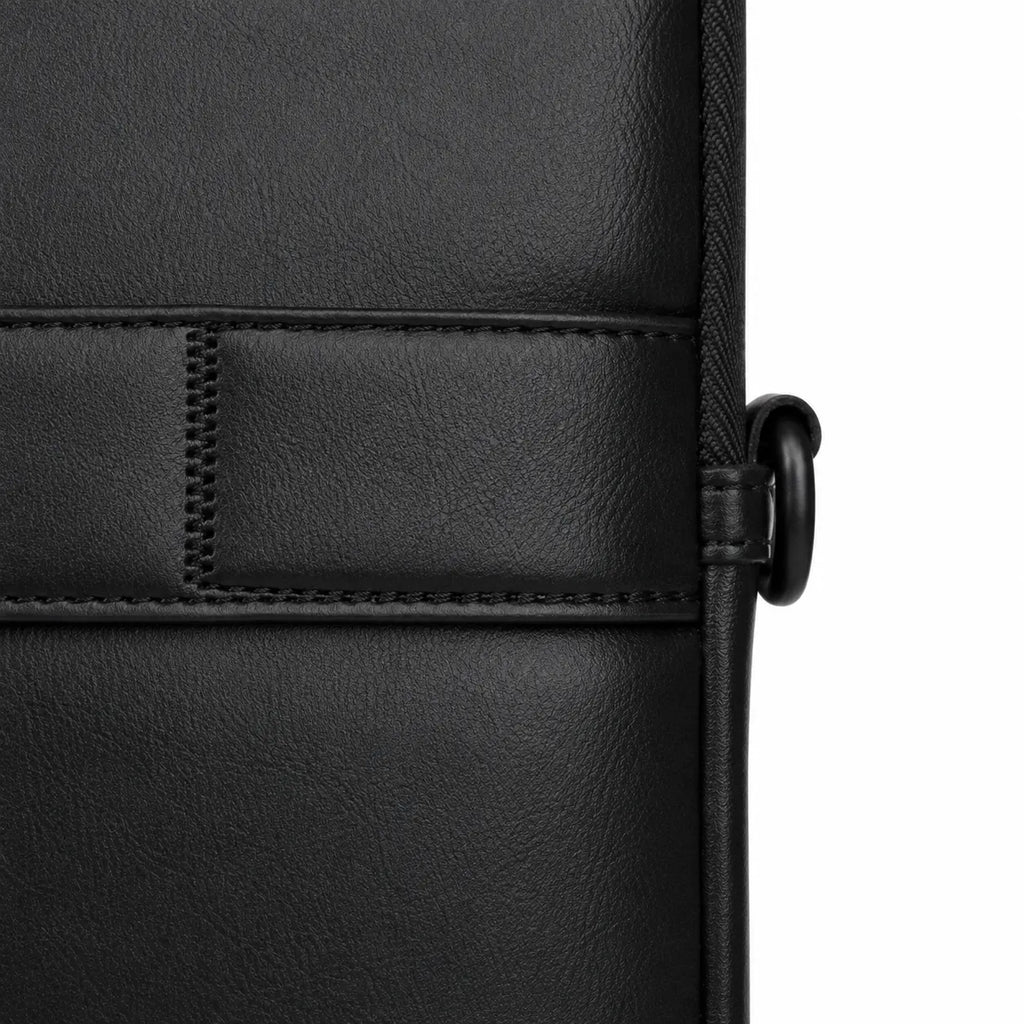 Close-up of a black textured leather or faux-leather bag corner with stitched paneling and a black strap ring on a white background.