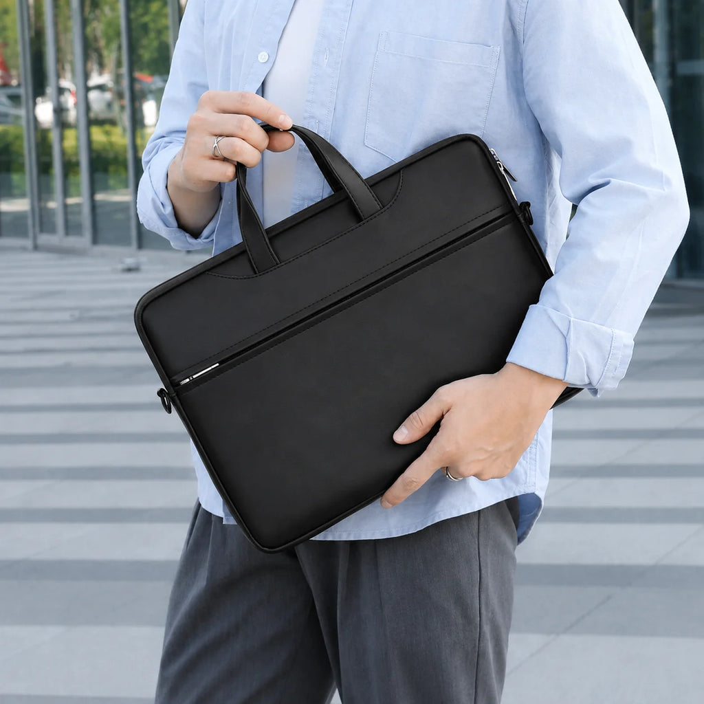A person in a light blue button-up shirt and gray trousers holds a black laptop briefcase with a top handle in an outdoor urban setting.
