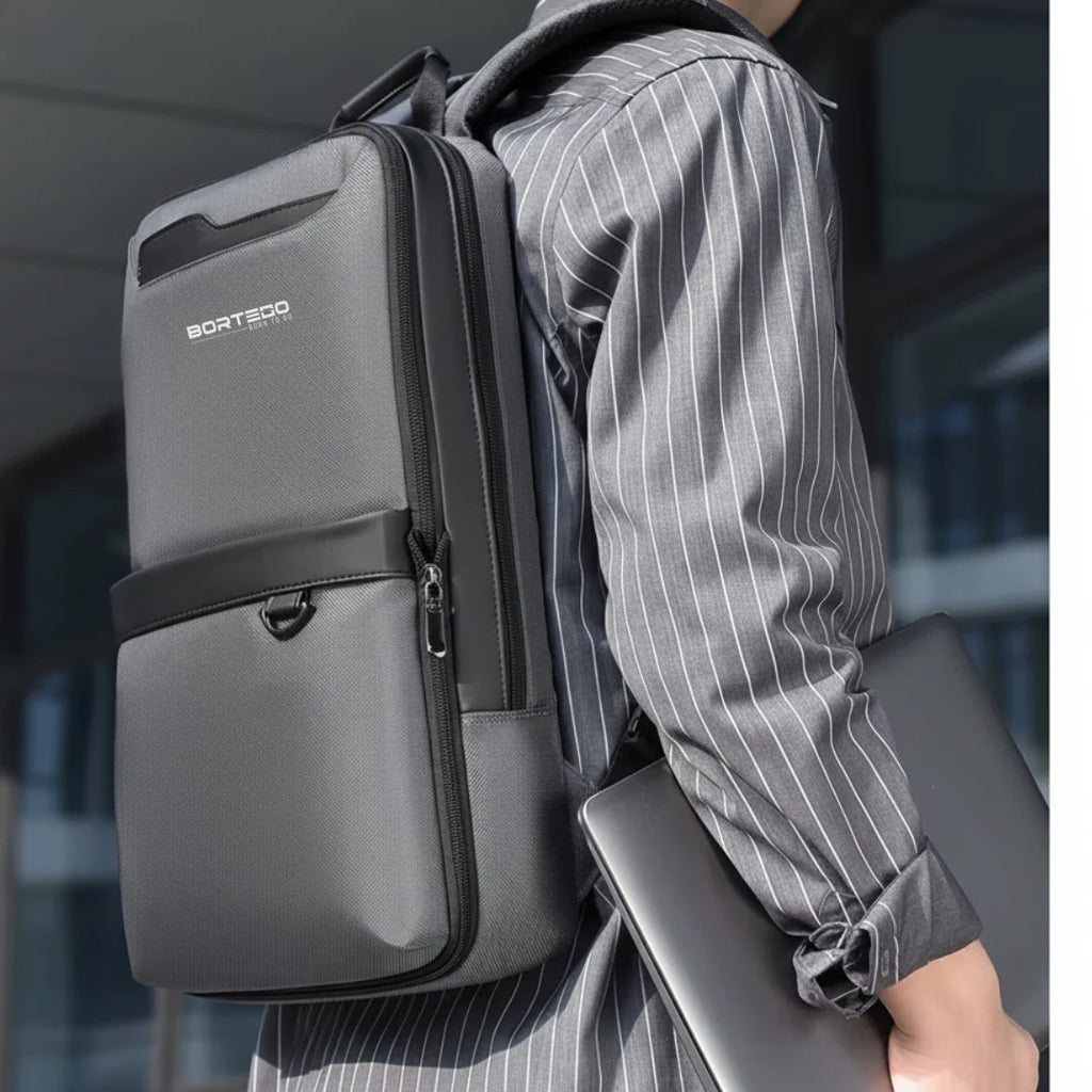 Person wearing a gray backpack with Bortego branding, holding a laptop.