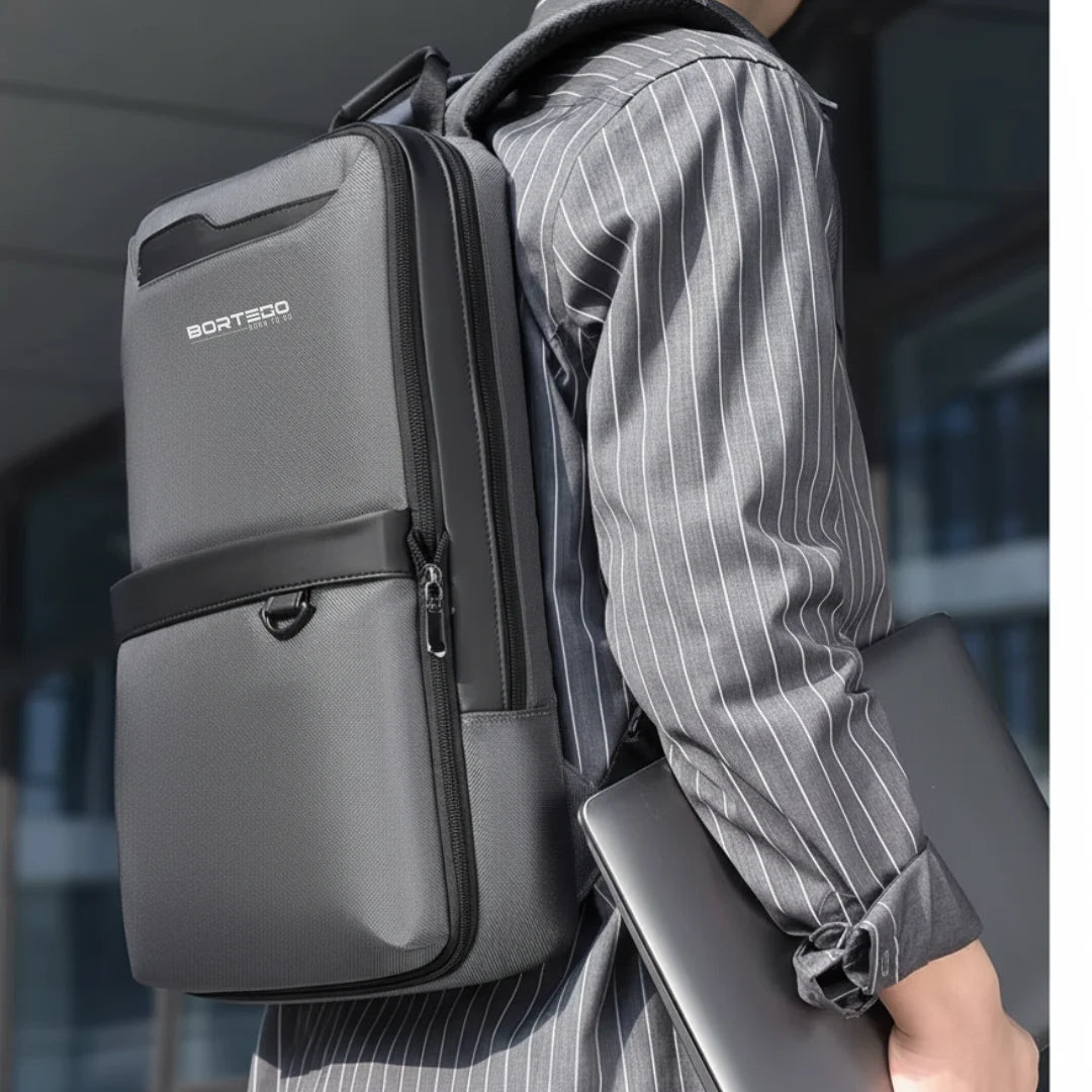 Person wearing a gray backpack with Bortego branding, holding a laptop.