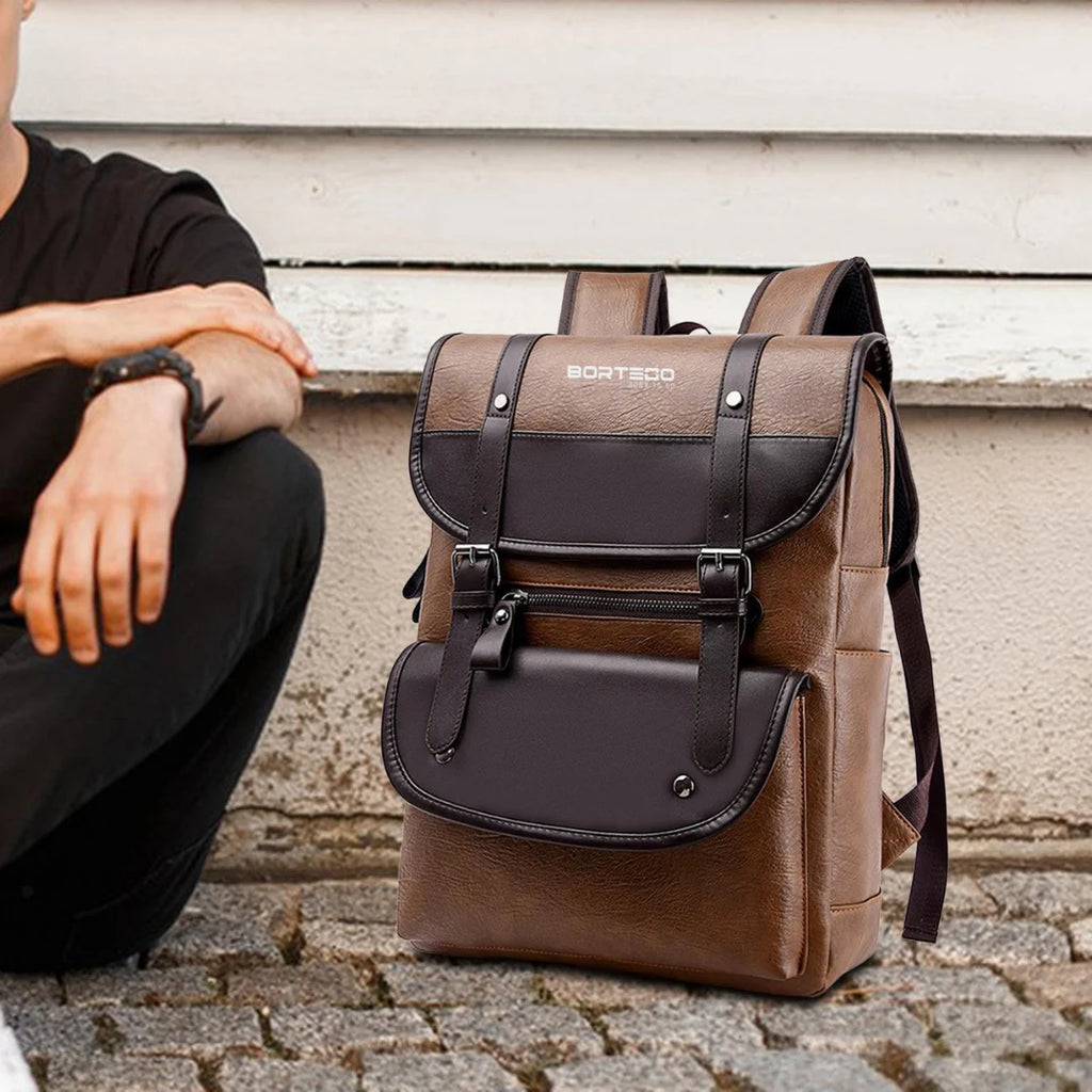 Brown backpack Bortego with black accents on a stone surface, person sitting nearby.