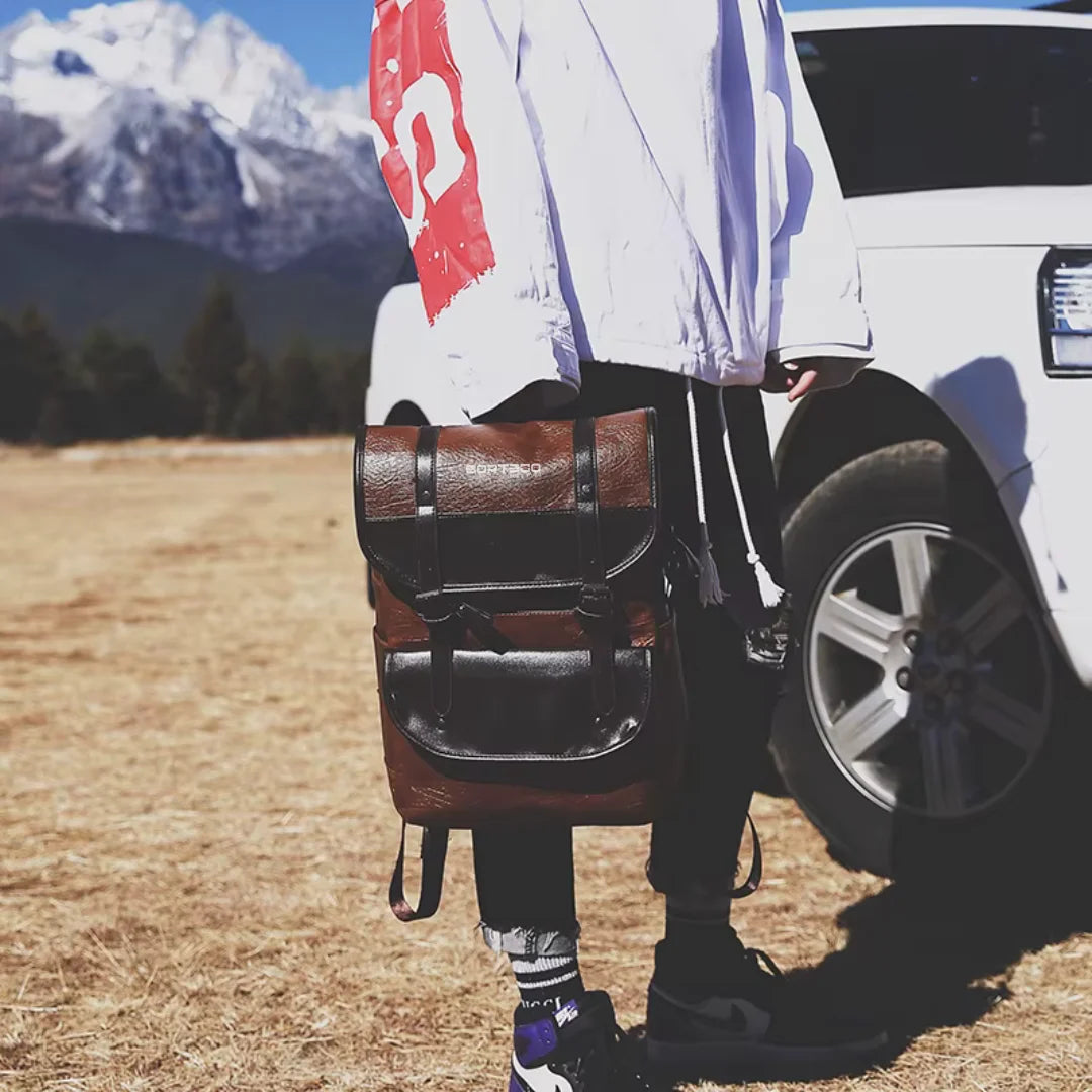 Person with a backpack Bortego standing next to a white SUV in a field with mountains in the background