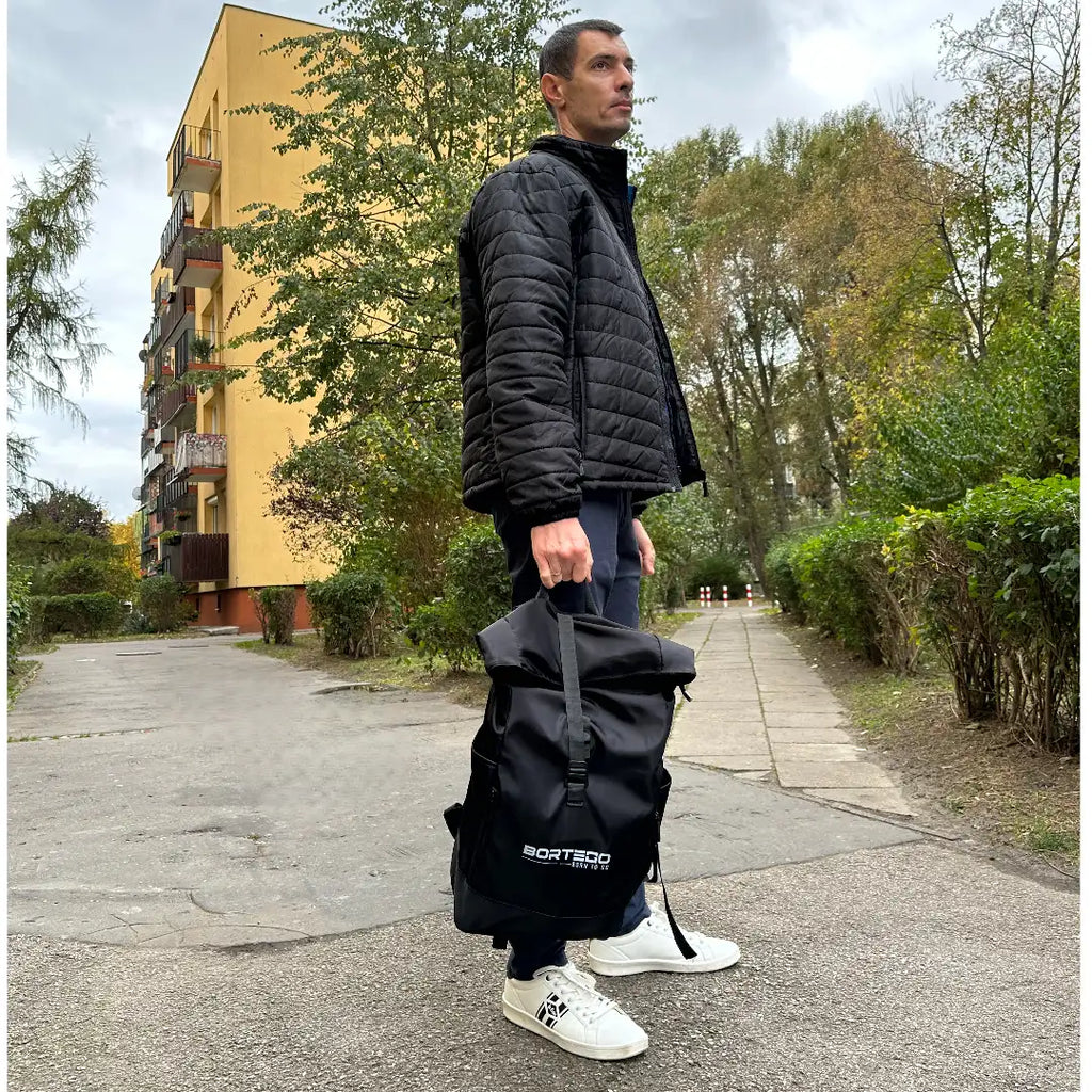 Man holding a black bag with a building and trees in the background