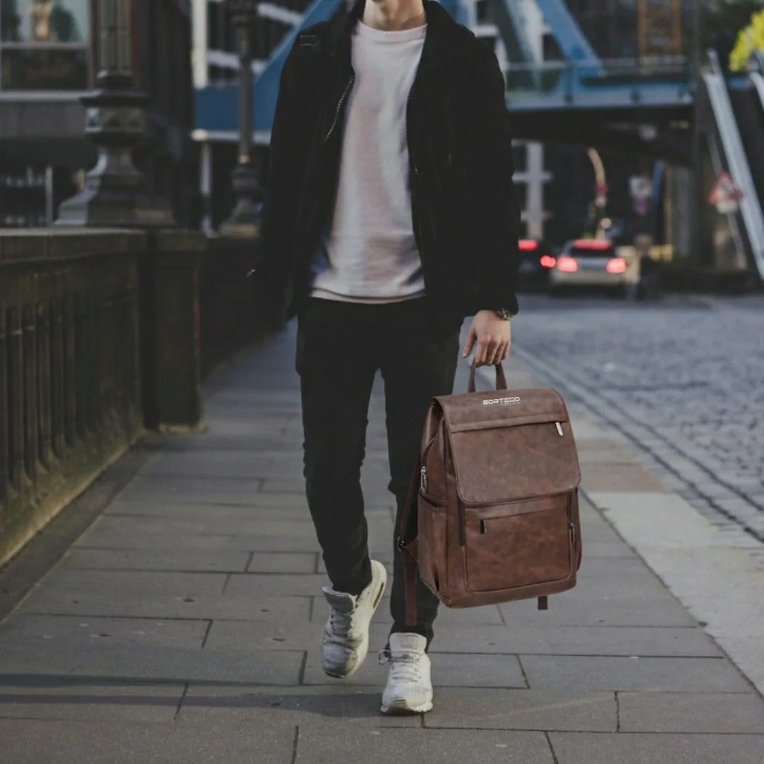 Person walking on a city street holding a brown backpack