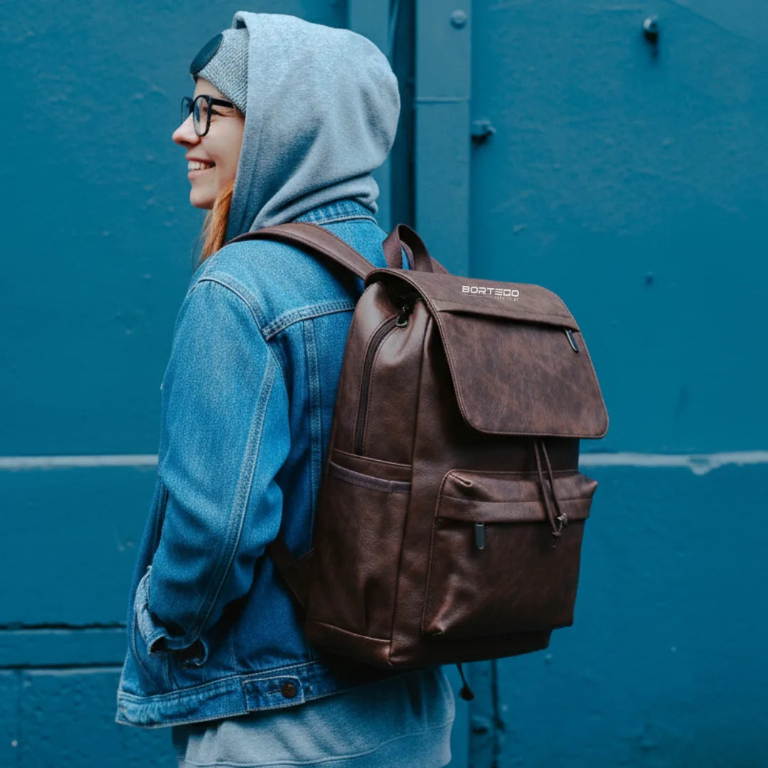 Person wearing a brown backpack with a visible brand logo against a blue wall.