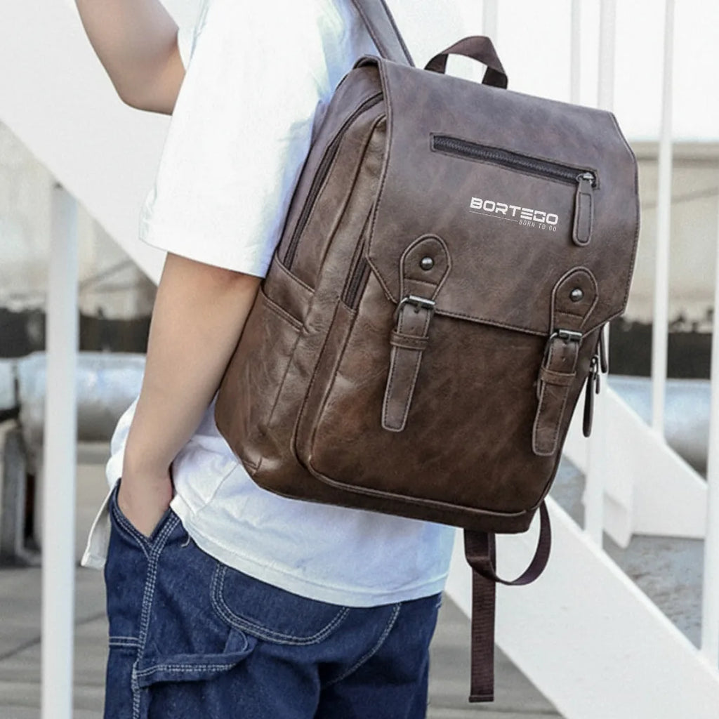 Brown leather backpack with 'Bortogo' branding held by a person on a white railing.