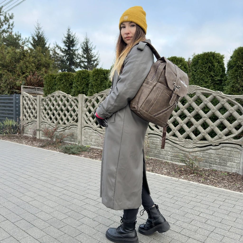 Person wearing a long coat, yellow beanie, and carrying a backpack on a paved walkway.